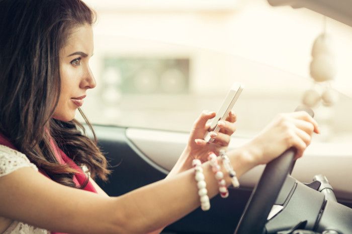 Young beautiful woman texting on a cell phone and waiting in the city traffic